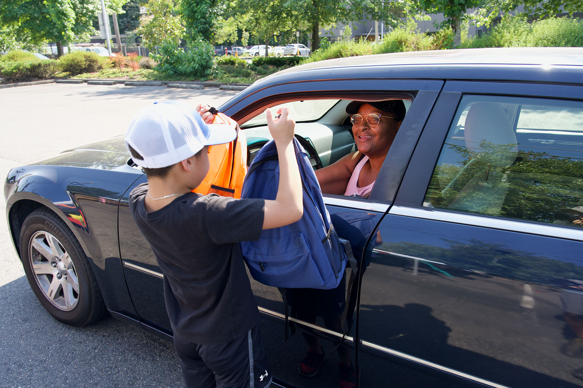 Kid showing two backpacks to a person in a black car