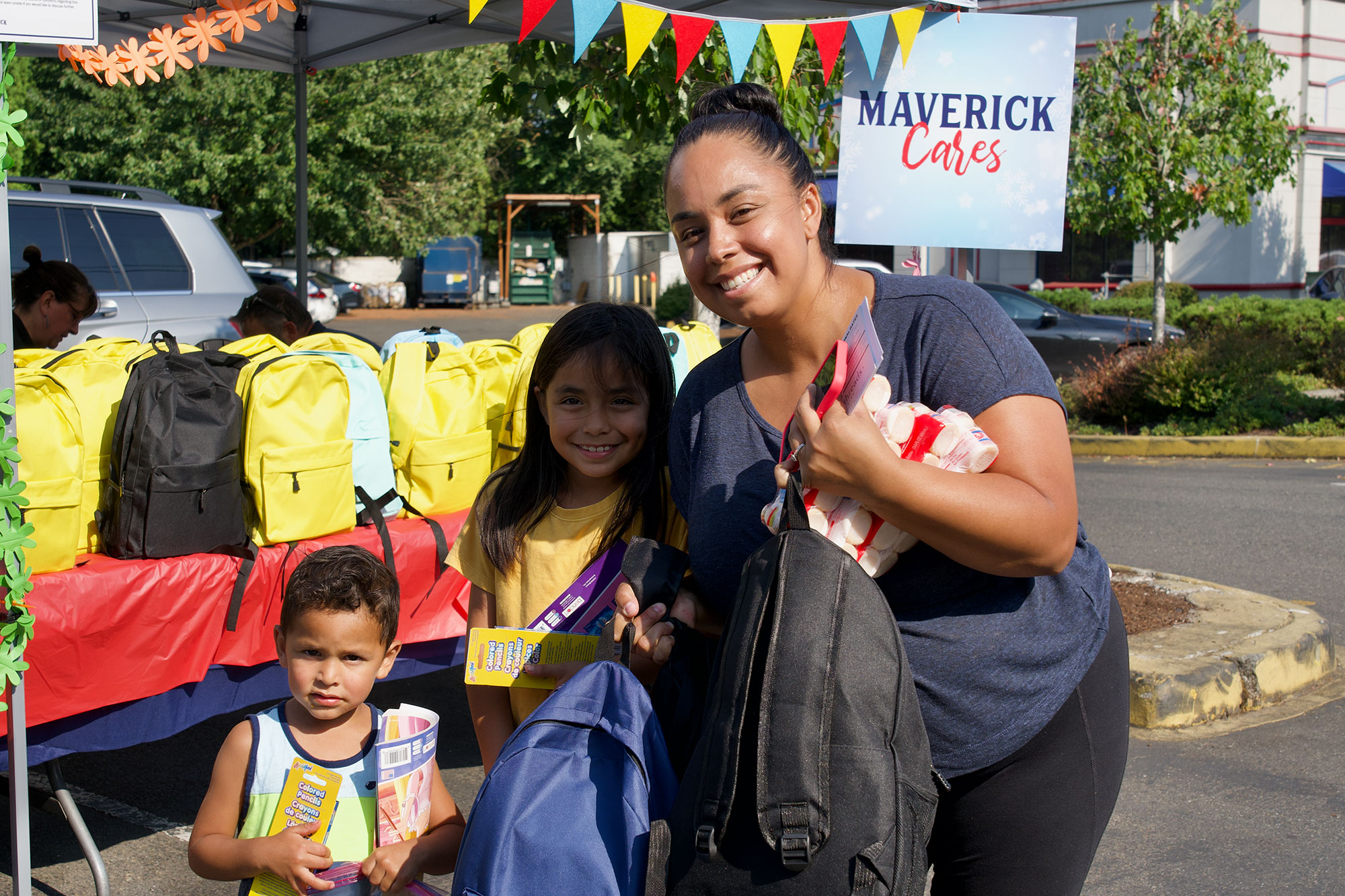 Woman with two kids smiling and holding two backpacks