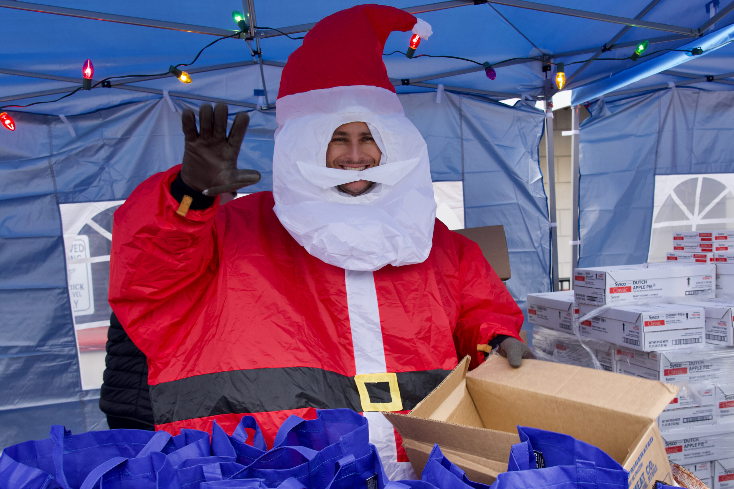 A man dressed like Santa Claus waving and holding a box in his hand